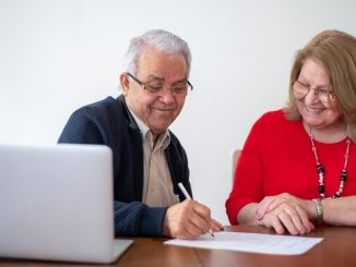 Un couple senior sourit en signant un document de location de studio avec un ordinateur portable