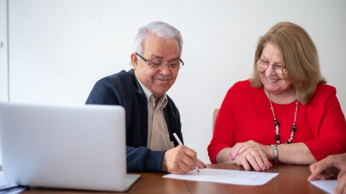 Un couple senior sourit en signant un document de location de studio avec un ordinateur portable