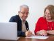 Un couple senior sourit en signant un document de location de studio avec un ordinateur portable
